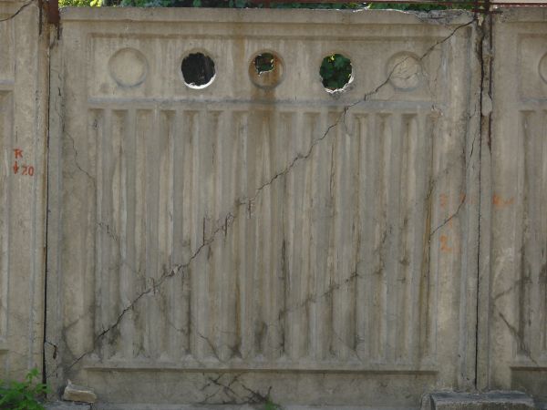 Concrete fence texture molded with a pattern of circles above vertical recessions, with large cracks and stains. The fence appears to be crumbling around the edges.